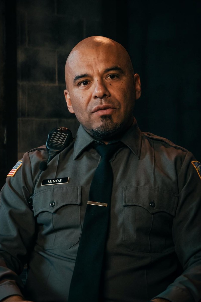 Luis Moncada as Minos, a corrections officer in his grey uniform
