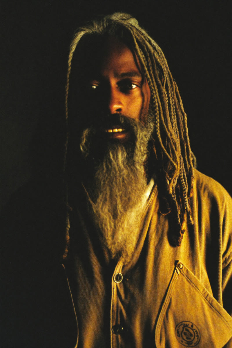 Concept portrait of Herald, a bearded long-haired man half in shadow